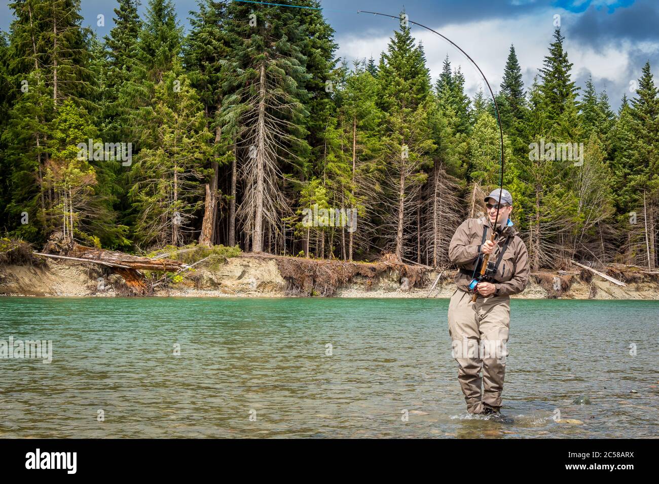Un pescatore di mosca di sport agganciato in un salmone sul fiume verde di Kitimat, nella Columbia Britannica, Canada, con il bosco di conifere in background. Foto Stock
