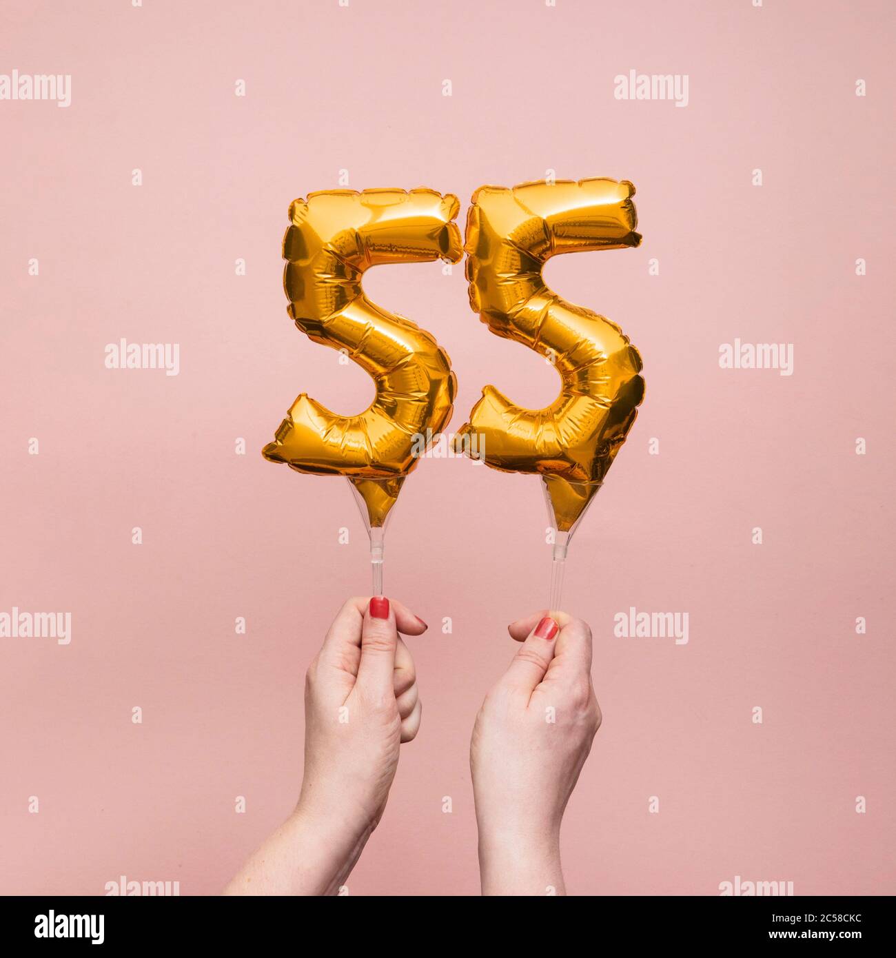 Mano femminile che tiene un numero 55 compleanno anniversario celebrazione palloncino oro Foto Stock