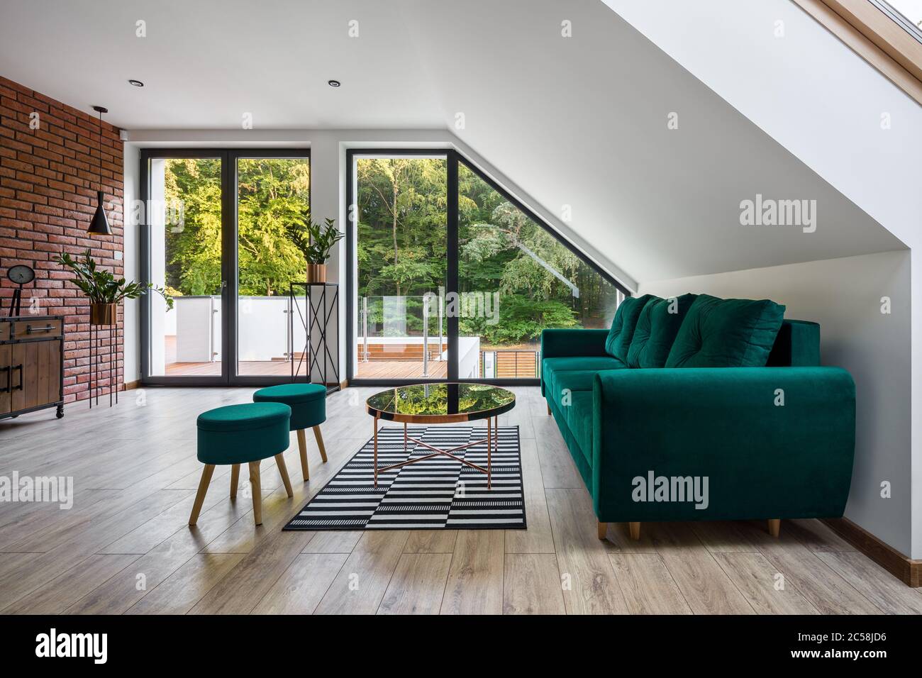 Elegante soggiorno attico con pareti in mattoni, mobili di verde smeraldo e pavimento in legno Foto Stock