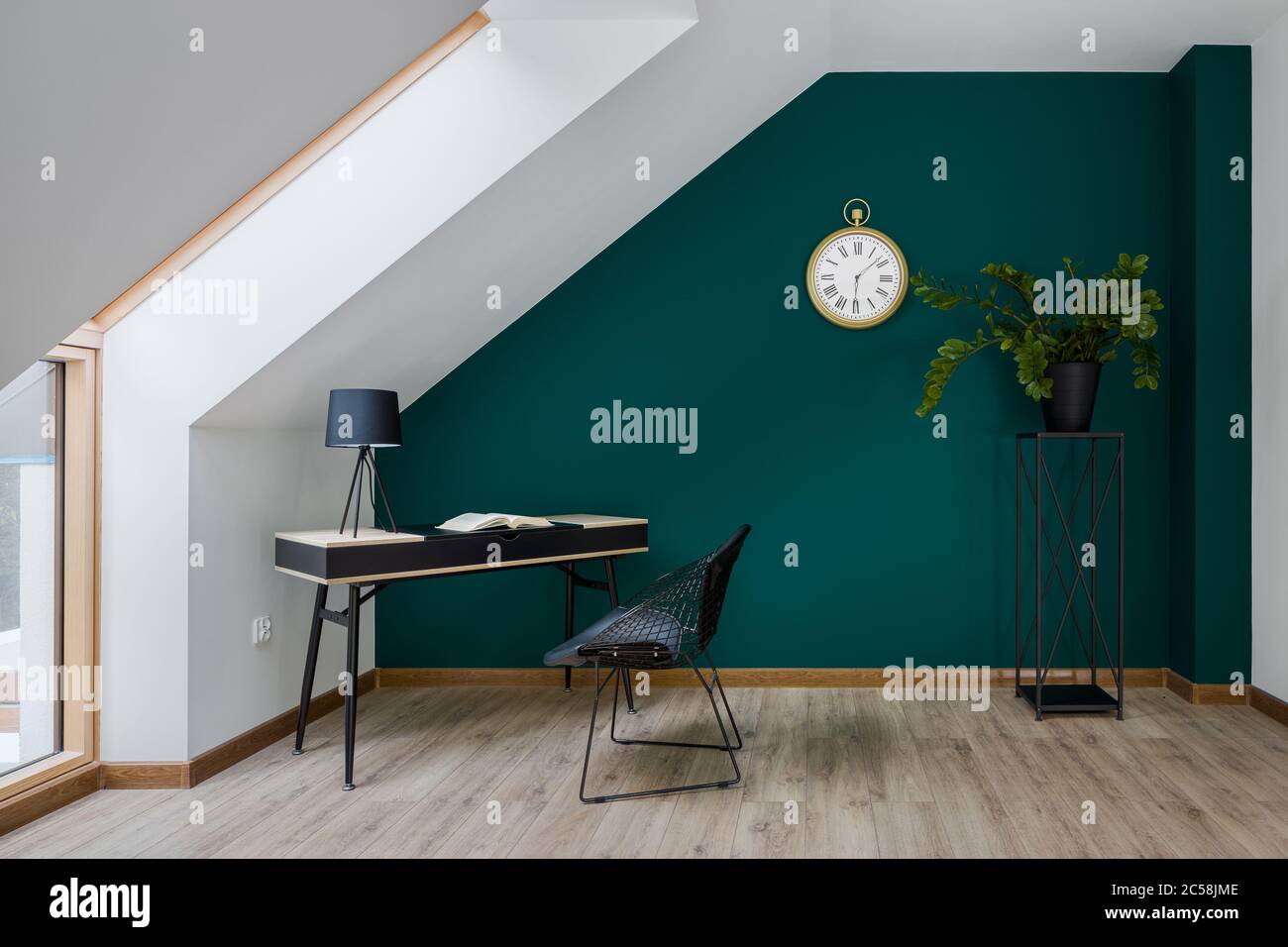Mansarda con parete color smeraldo, grande finestra, elegante scrivania con sedia Foto Stock