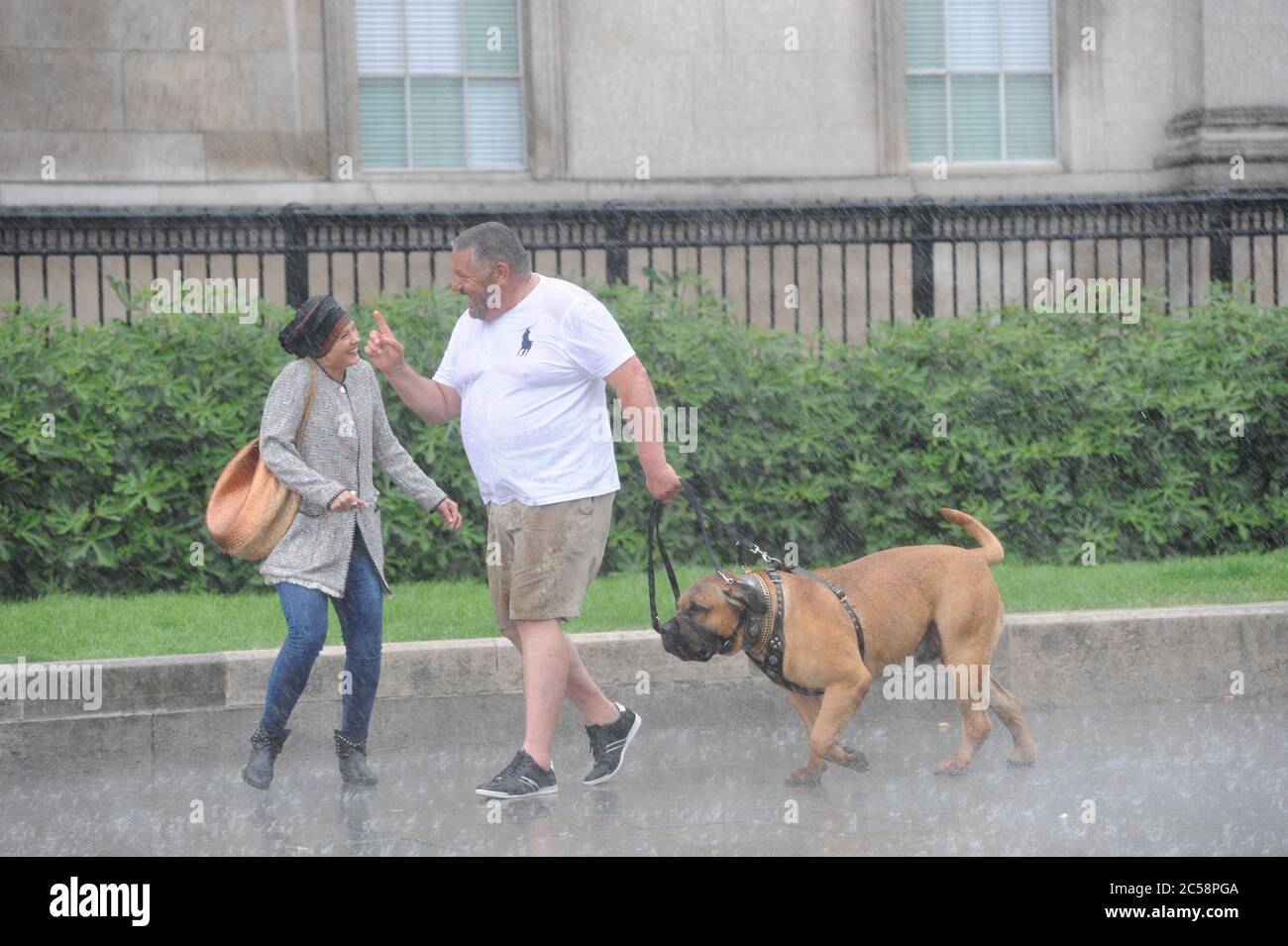 Londra, UK, 1 luglio 2020 coppia con cane catturato in doccia pesante che attraversa Trafalgar Square non lasciarlo scendere. Pioggia in Trafalgar Square il primo giorno di luglio. Credit: JOHNNY ARMSTEAD/Alamy Live News Foto Stock