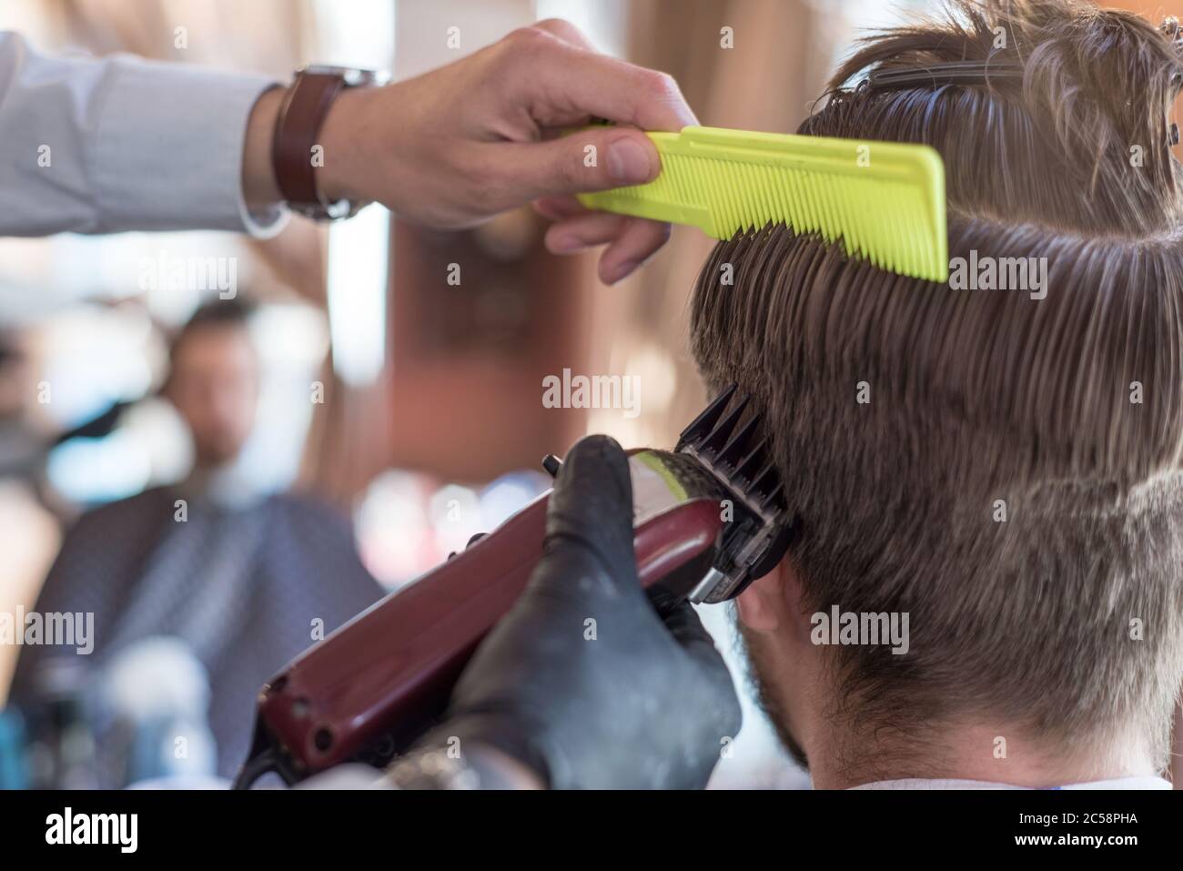 un parrucchiere taglia un giovane ragazzo con un rifinitore per capelli, pettinando i capelli sulla sua testa. Lavoro del maestro nel taglio di capelli degli uomini in un barbiere Foto Stock