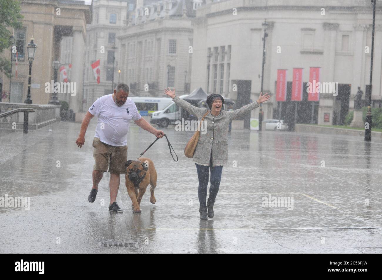 Londra, UK, 1 luglio 2020 coppia con cane catturato in doccia pesante che attraversa Trafalgar Square non lasciarlo scendere. Pioggia in Trafalgar Square il primo giorno di luglio. Credit: JOHNNY ARMSTEAD/Alamy Live News Foto Stock