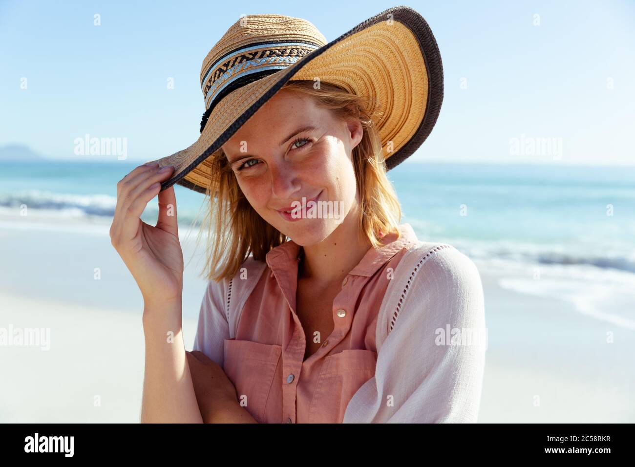 Ritratto di donna che indossa cappello sorridente sulla spiaggia Foto Stock