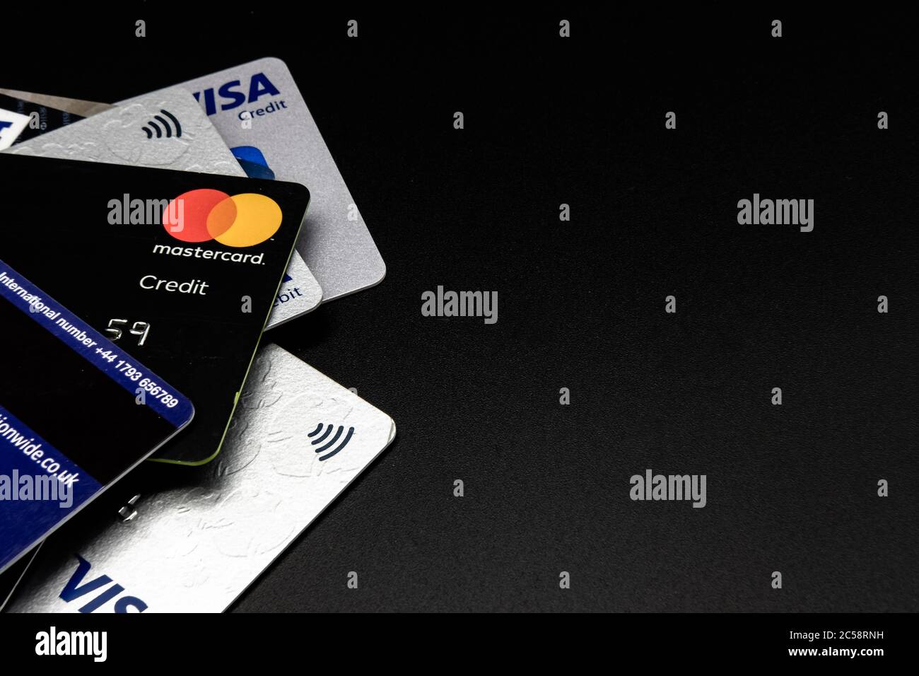 Pila di carte di credito e di debito di ben note società finanziarie. Visualizzazione dei dettagli dei disegni insieme ai simboli di pagamento senza contatto. Foto Stock