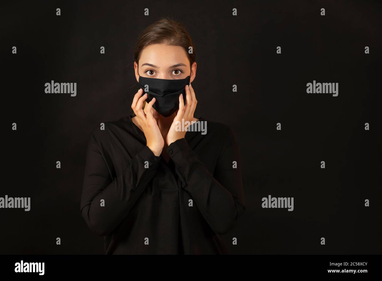 Giovane donna bruna che tocca il viso in maschera protettiva. Foto Stock