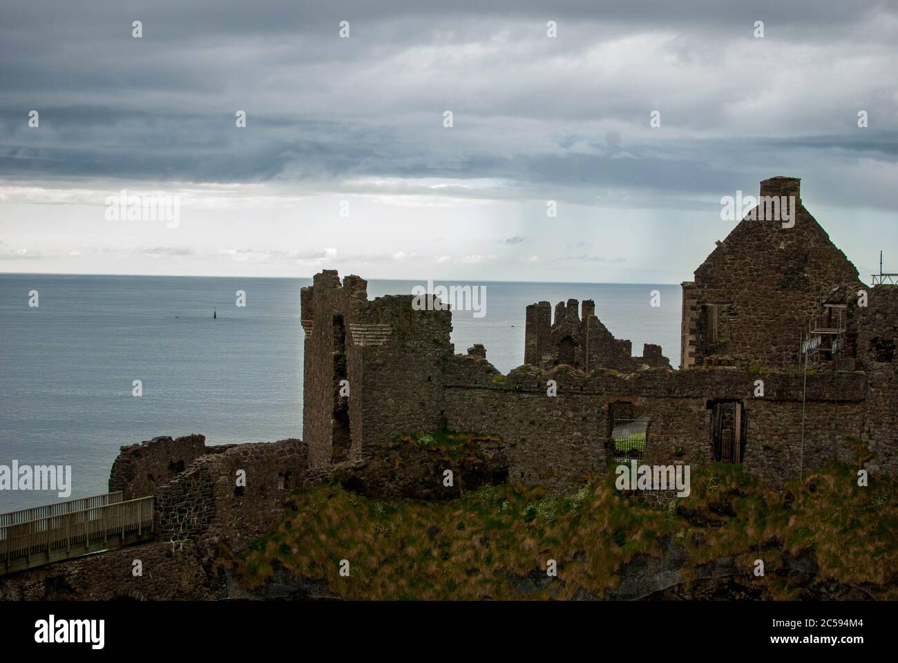 Il Castello di Dunluce circondato dal mare, dalle rocce e dalle giornate nuvolose con la pioggia sul suo cammino. Foto Stock