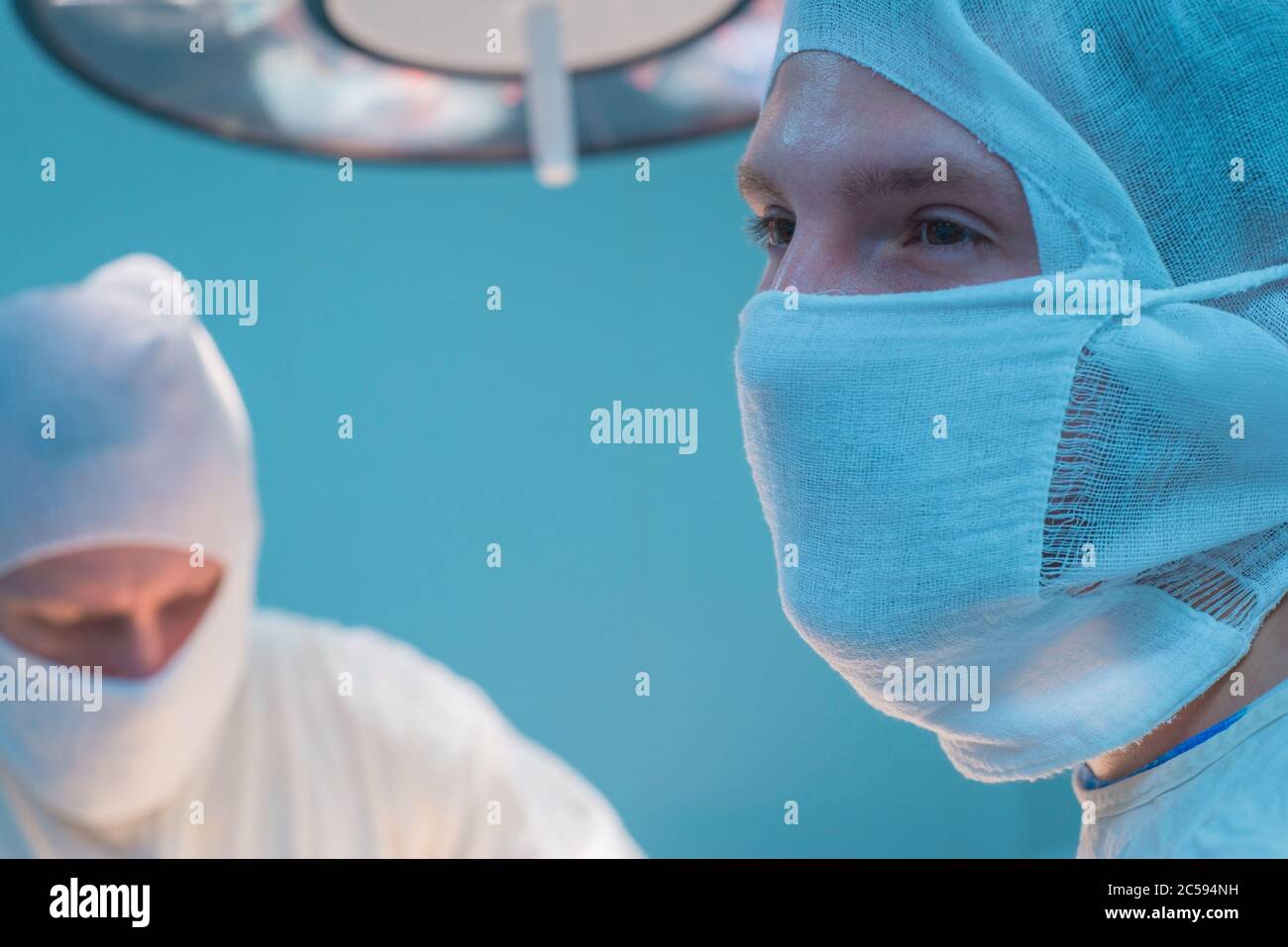 primo piano dei chirurghi in maschera sterile, sullo sfondo di una lampada operatrice, con le mani sollevate, l'assistente del chirurgo guarda Foto Stock
