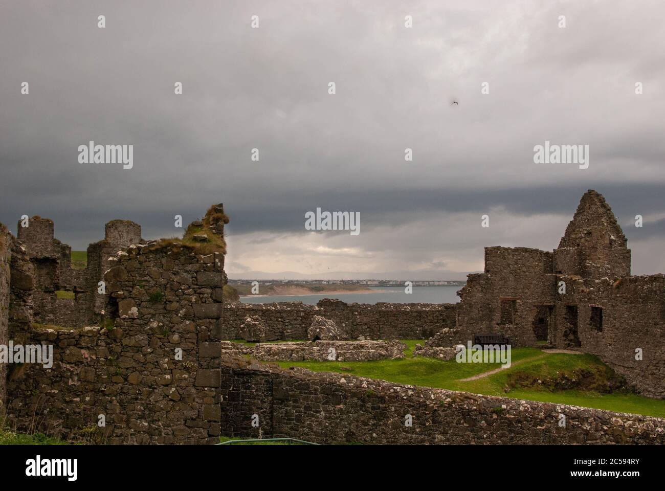 Il Castello di Dunluce circondato dal mare, dalle rocce e dalle giornate nuvolose con la pioggia sul suo cammino. Foto Stock