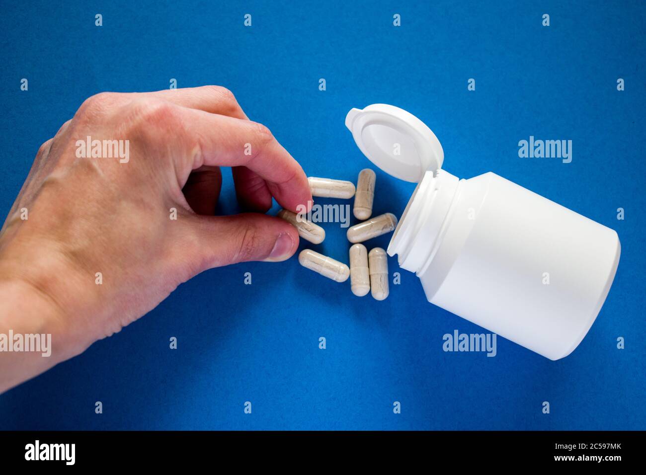 Donne mano che prende la pillola medica da flacone di pillola versato su sfondo blu Foto Stock