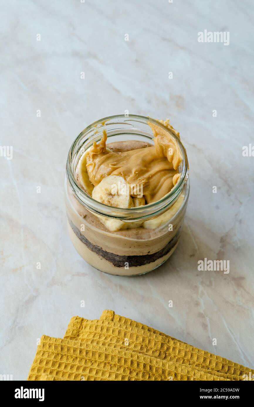 Torta di burro di arachidi cremosa Dessert con fetta di banana e torta al cioccolato in vaso / tazza di dieta Paleo. Cibo sano e biologico fatto in casa. Foto Stock