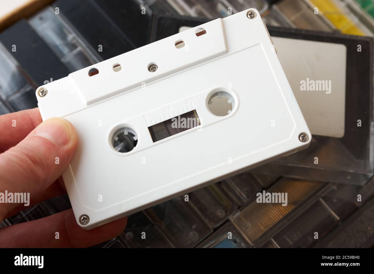 Le dita maschio tengono la cassetta audio bianca senza segni. Scatola con nastri sullo sfondo. Primo piano Foto Stock