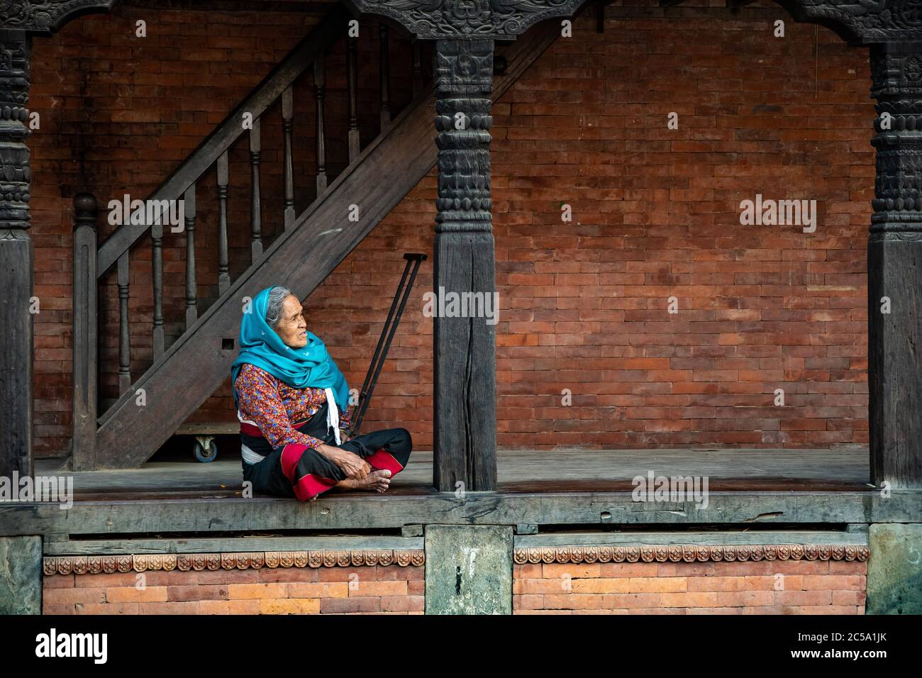 Anziana donna nepalese seduta sulla veranda della sua tipica casa in stile Newa a Bhaktapur, Nepal Foto Stock