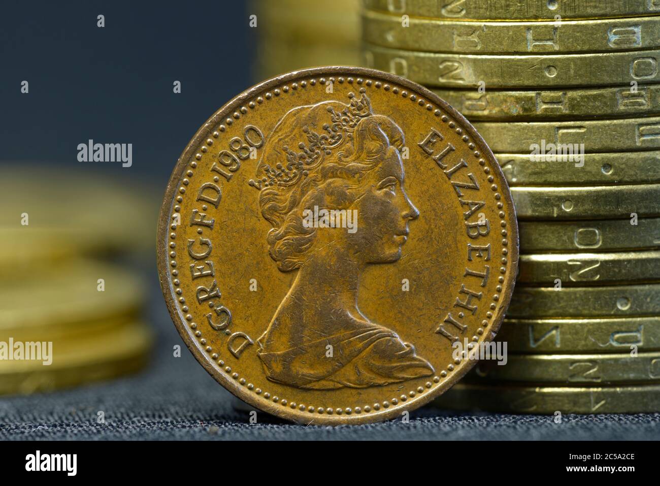 Una vecchia moneta da 1980 anni con ritratto della regina Elisabetta II messa sul bordo davanti a pile di monete Foto Stock