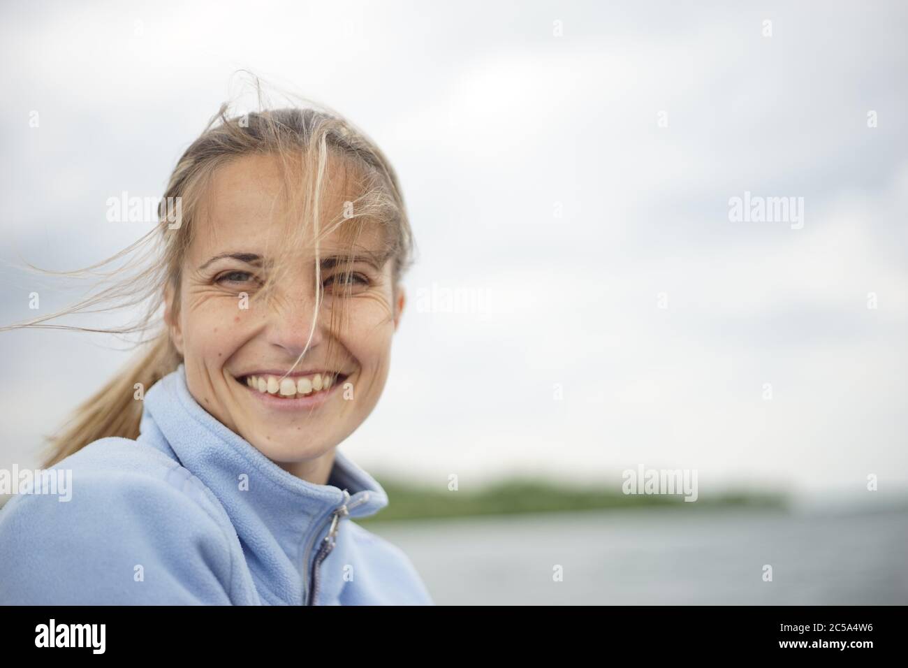 Un ritratto di una donna nel suo 20s/30s.She sta sorridendo e guardando la macchina fotografica. Sullo sfondo, si potrebbe vedere un corpo di acqua - lago, fiume, mare, ecc Foto Stock