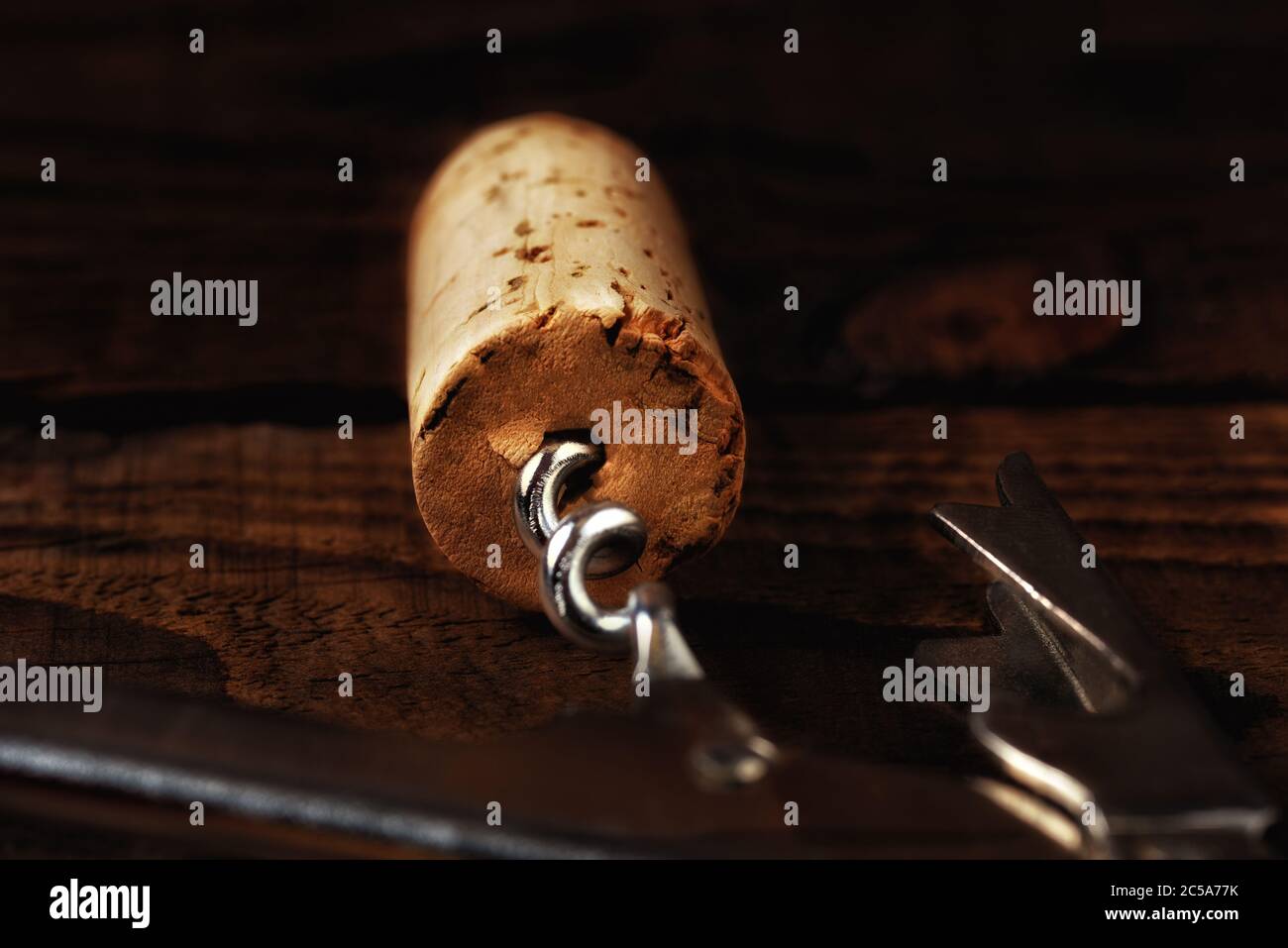 Chiusura di un tappo di sughero e cavatappi su un tavolo di legno scuro, con forte luce laterale. Profondità di campo poco profonda con fuoco sull'estremità del sughero. Foto Stock