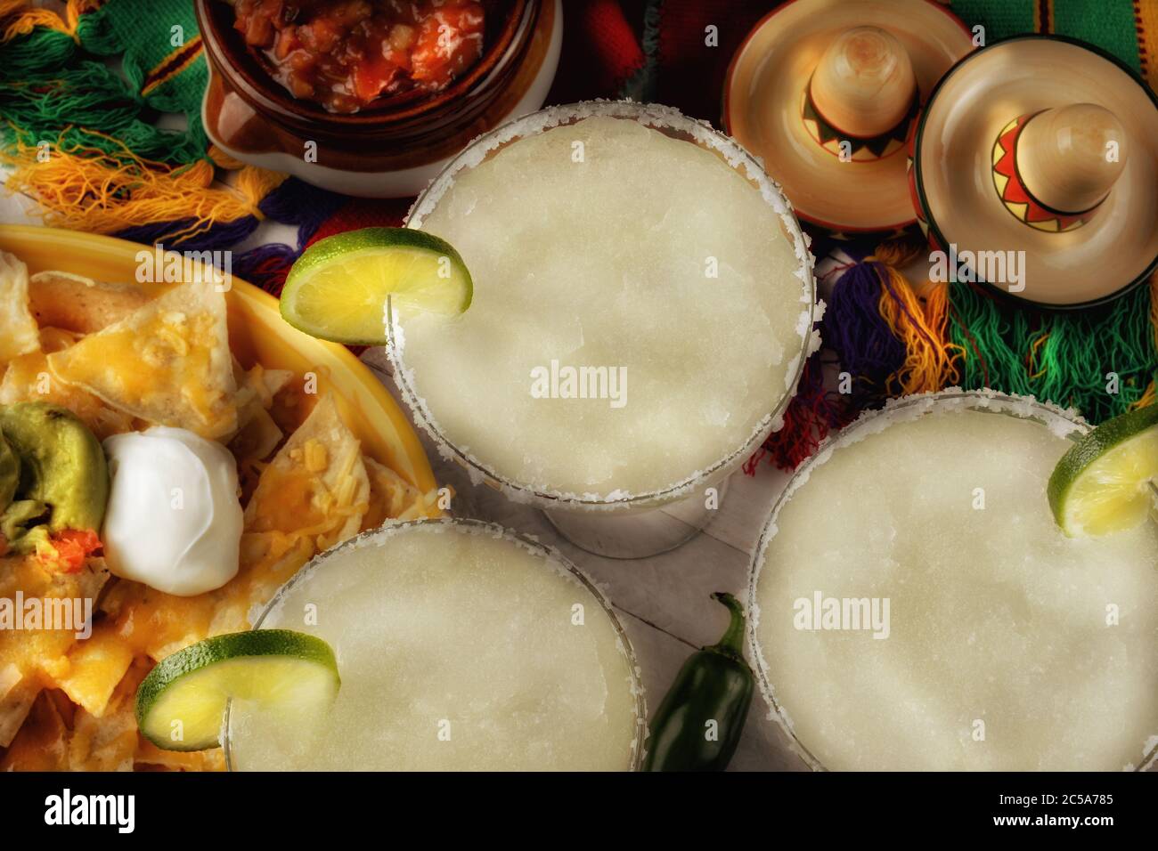Vista ad alto angolo di tre cocktail margarita circondati da nachos, patatine e salsa su un luminoso telo da tavolo messicano. Formato orizzontale. Perfetto per ci Foto Stock