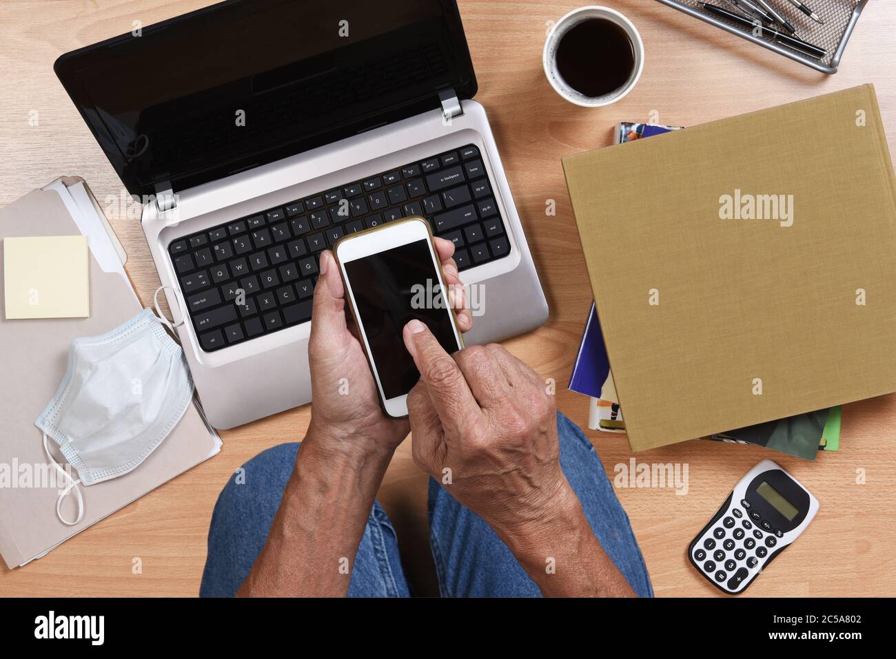 Uomo inginocchiato sul pavimento lavorando da casa con il suo portatile cellulare, libri, caffè e altri oggetti per il telecommuto durante il COVID-19 soggiorno a casa Foto Stock