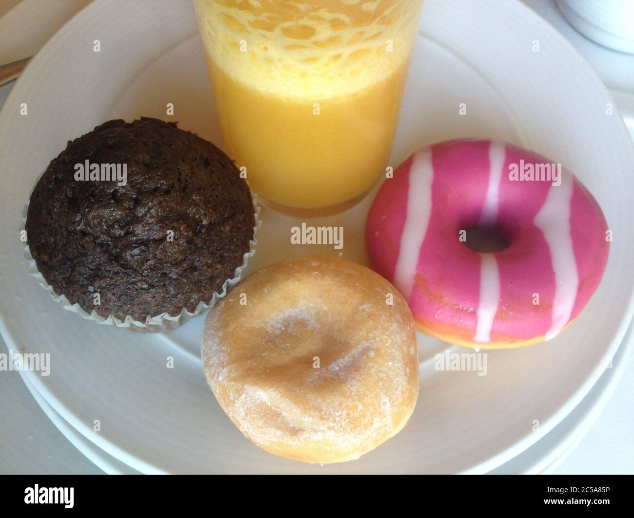 Colazione malsana e super dolce. Diverse torte intorno al bicchiere di succo d'arancia Foto Stock