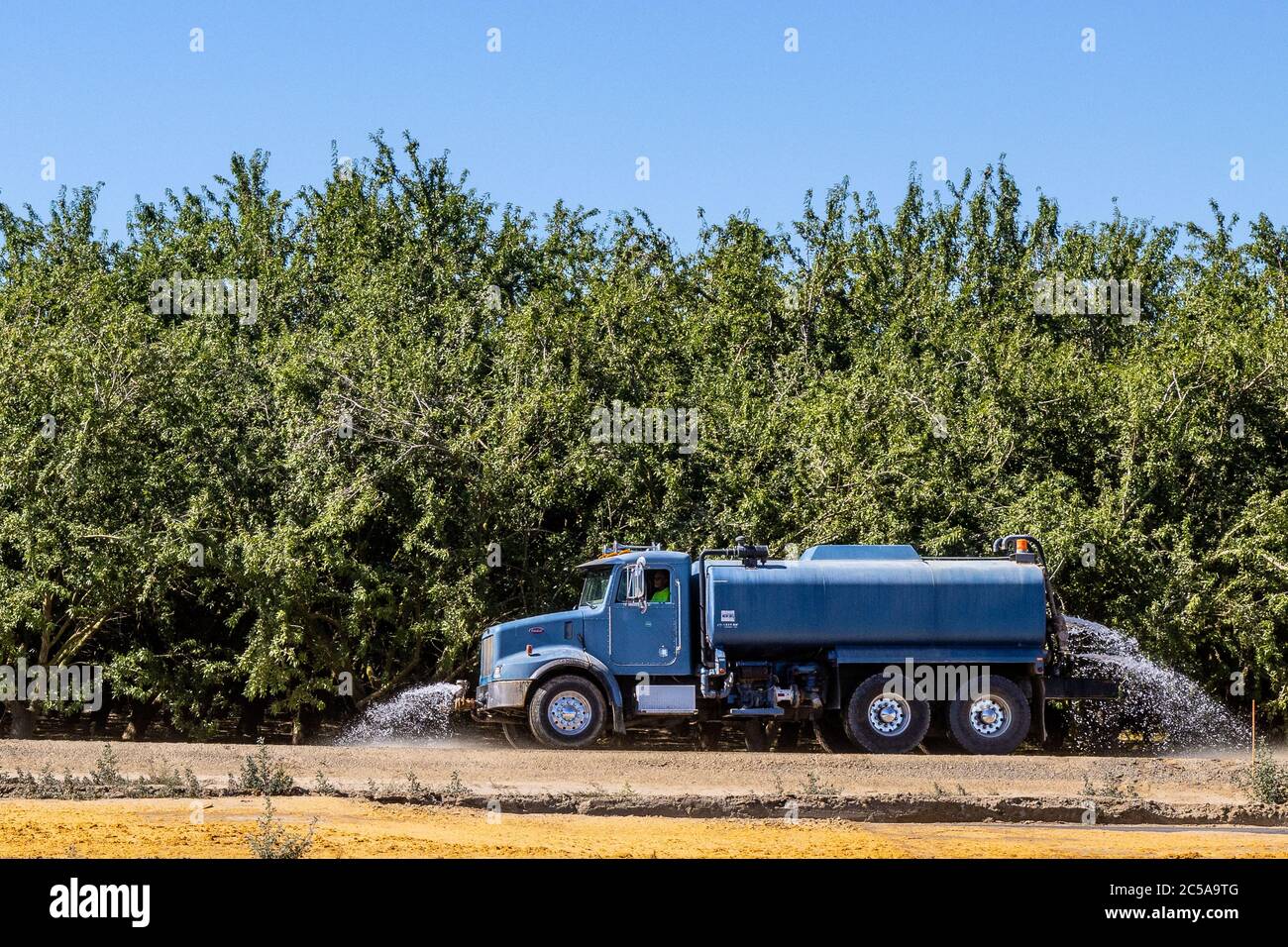 Un camion ad acqua spruzzi giù il nuovo letto della strada per il reinstradamento dell'autostrada 132 in Modesto California USA Foto Stock