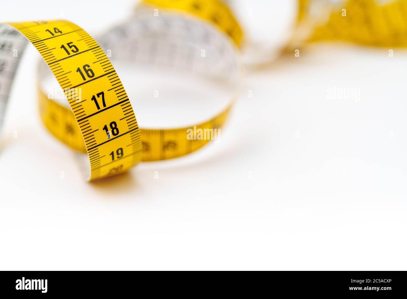 Nastro di misurazione giallo su sfondo bianco. Misurazione della lunghezza e della circonferenza. Perdere peso e ottenere grasso. Foto Stock