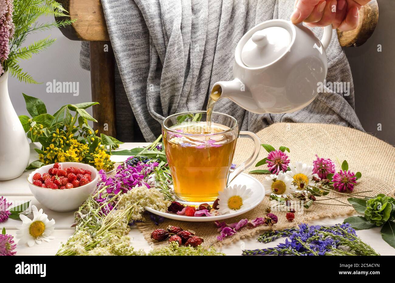 Una donna versa il tè alle erbe con camomilla, roseanca, trifoglio. Cerimonia del tè. Drink estivo Foto Stock