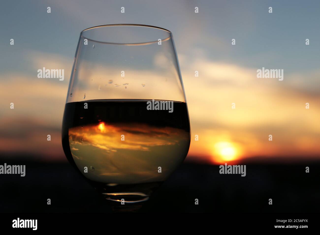 Vetro con vino bianco sul bellissimo tramonto sfondo, sole e cielo e vengono riflesse in alcool bere. Concetto di celebrazione, serata festa al resort Foto Stock