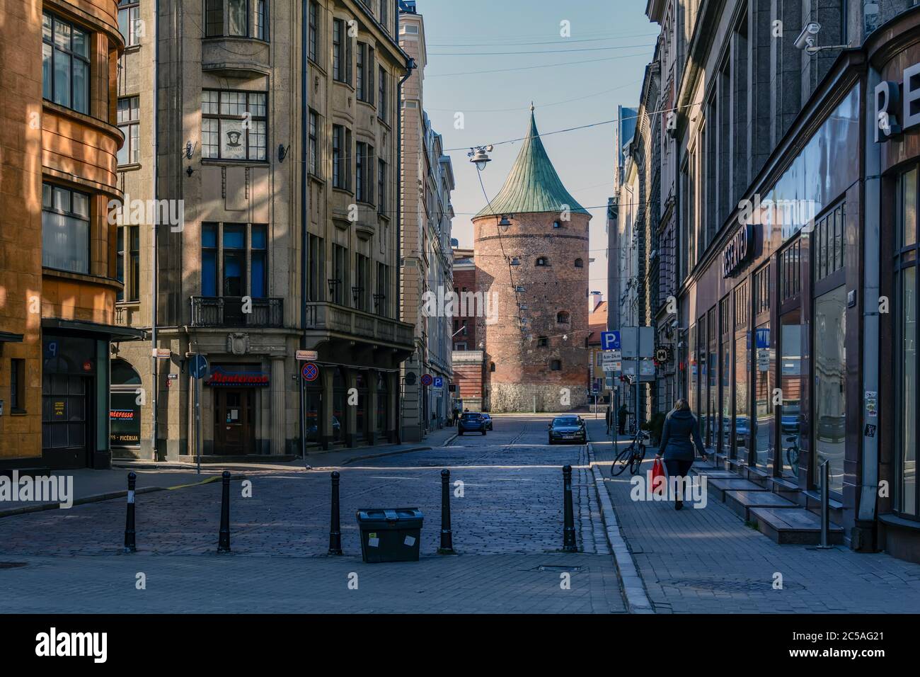 A poche persone in una strada vuota della Città Vecchia di riga con la Torre medievale delle polveri Foto Stock