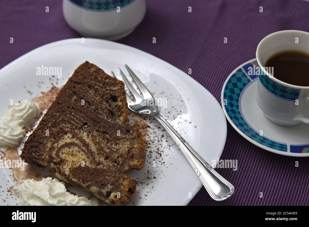 Un piatto con una fetta di zebra o torta di tigre, una panna montata e una tazza di caffè su una superficie viola Foto Stock