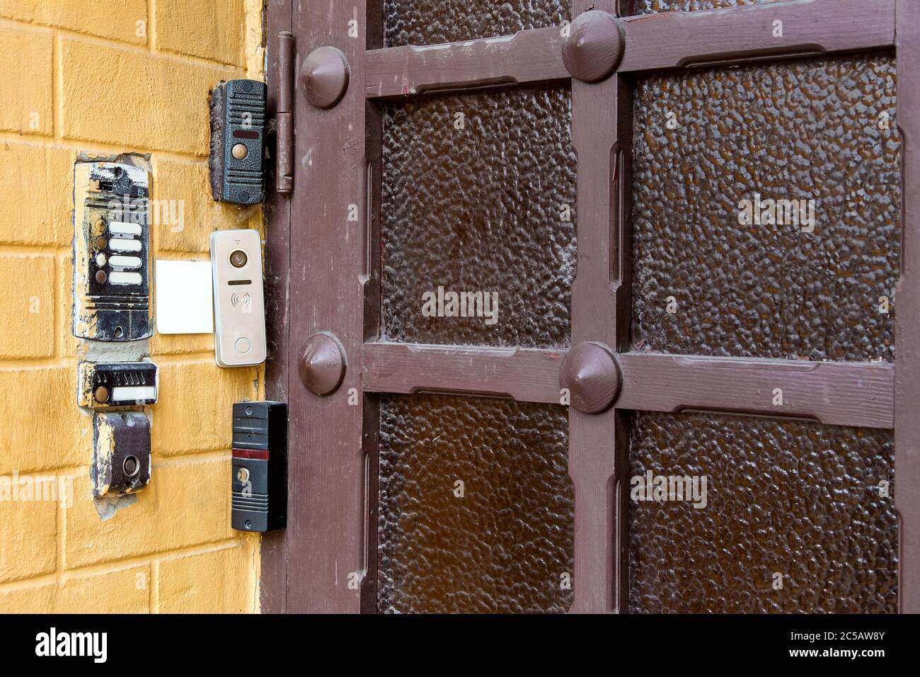 diversi intercom e serrature elettroniche su un chip o scheda su parete in mattoni all'aperto contro una porta di legno con vetro, closeup controllo di sicurezza remoto t Foto Stock
