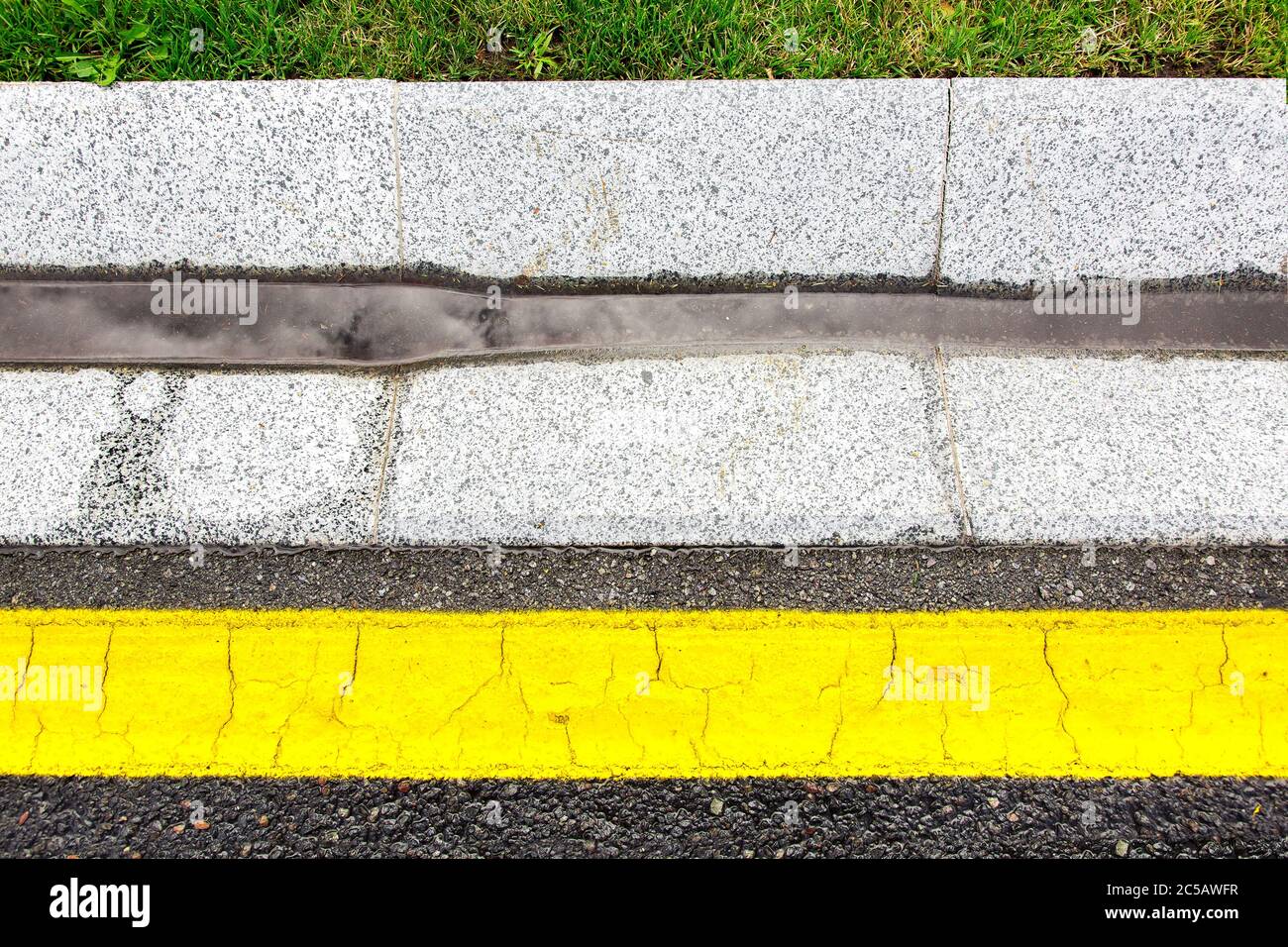canale acqua tempesta gocciolatoio in calcestruzzo con precipitazioni sul lato della strada asfaltata con segnaletica gialla vista dall'alto. Foto Stock