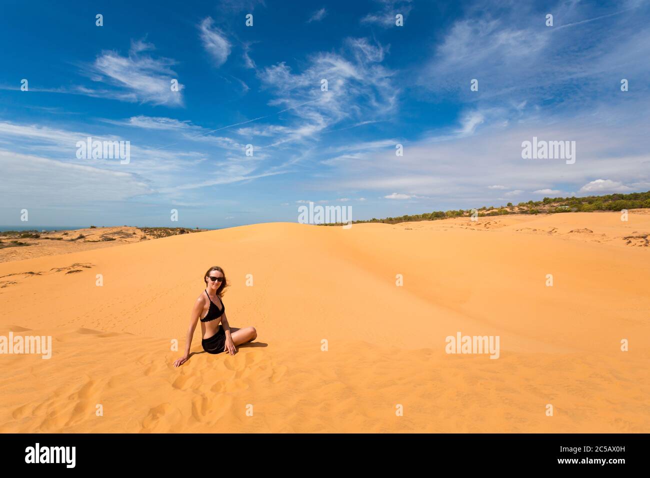 Bella ragazza caucasica che si diverte sulle dune di sabbia rossa a Mui NE, Phan Tiet zona in Vietnam. Paesaggio con cielo blu durante la giornata di sole. Foto Stock