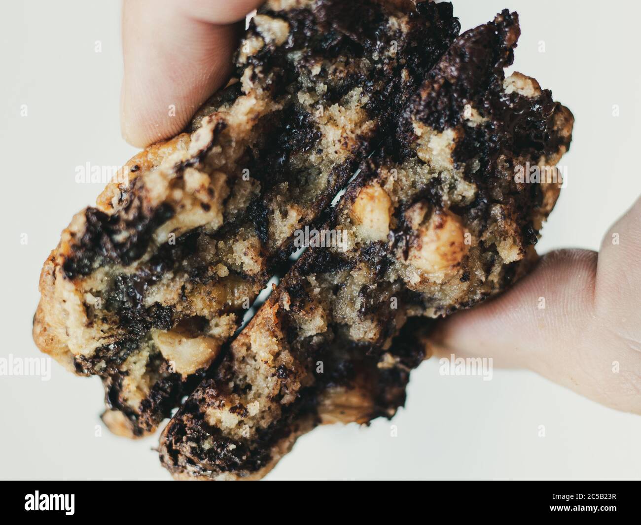 Primo piano dell'interno di due biscotti di farinata d'avena al cioccolato fondente tenuto dalle dita su uno sfondo bianco Foto Stock