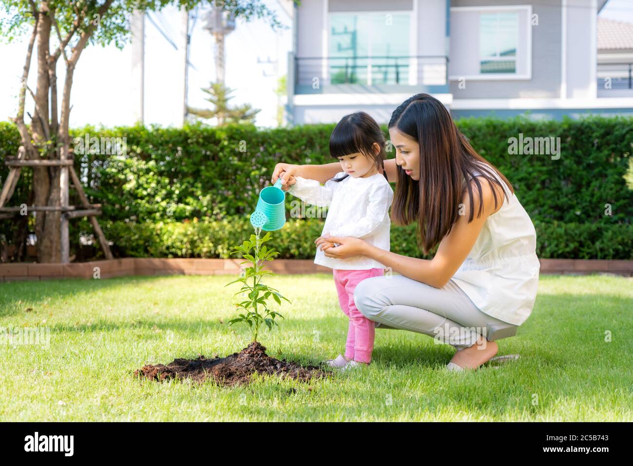 La madre asiatica della famiglia e la pianta della figlia del capretto che sellano l'albero ed innaffiando all'aperto nella molla della natura per ridurre la caratteristica di sviluppo di riscaldamento globale e prenda la cura Foto Stock