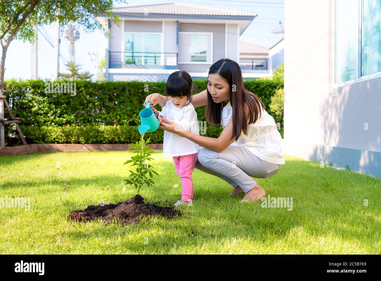 La madre asiatica della famiglia e la pianta della figlia del capretto che sellano l'albero ed innaffiando all'aperto nella molla della natura per ridurre la caratteristica di sviluppo di riscaldamento globale e prenda la cura Foto Stock