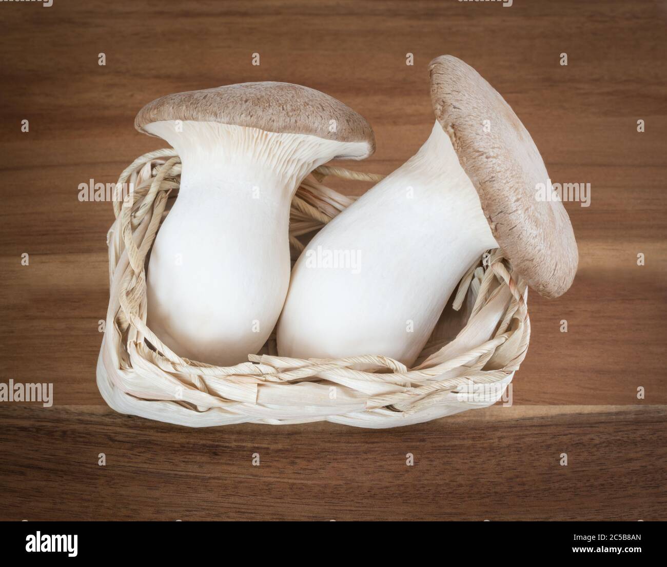 Due funghi in un piccolo cesto su una tavola di legno Foto Stock