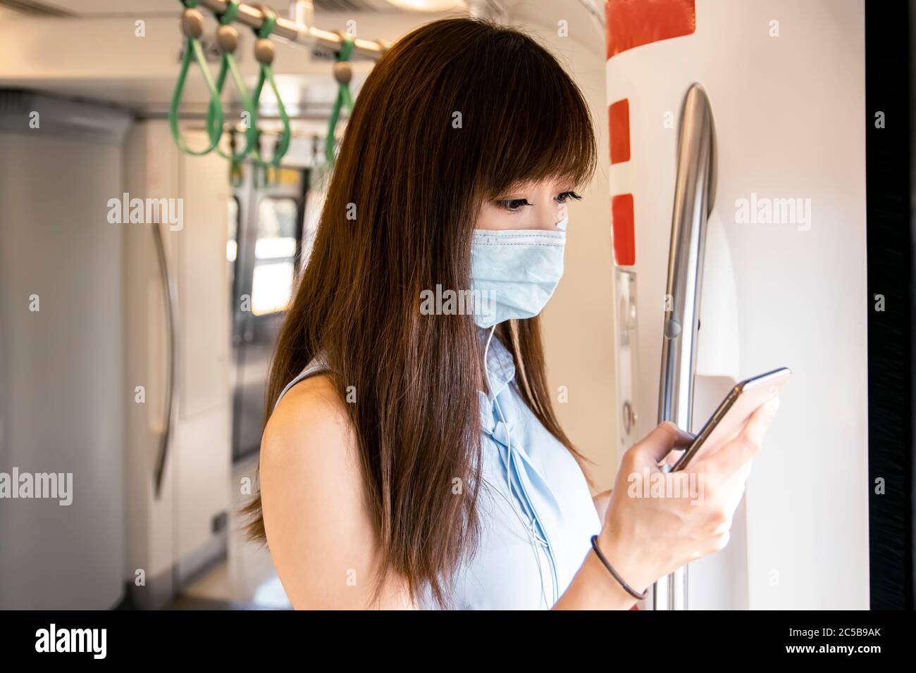 Giovane donna asiatica passeggero indossando maschera chirurgica e ascoltando musica tramite telefono cellulare in treno della metropolitana Foto Stock