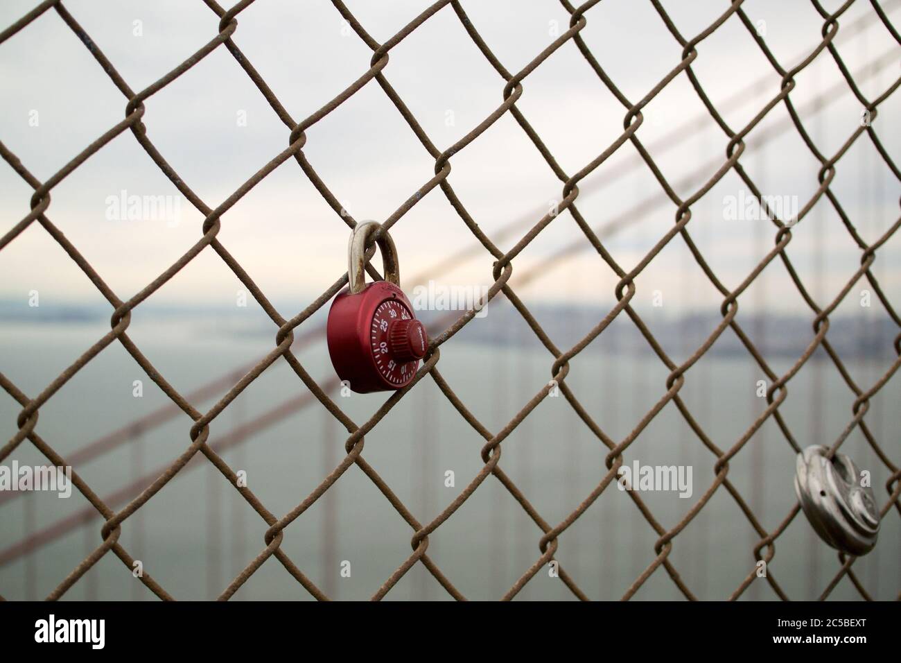 Lucchetti d'amore sul Golden Gate Bridge, una serratura a combinazione rossa, un lucchetto rotondo. Skyline di San Francisco sullo sfondo. Cielo grigio. Foto Stock