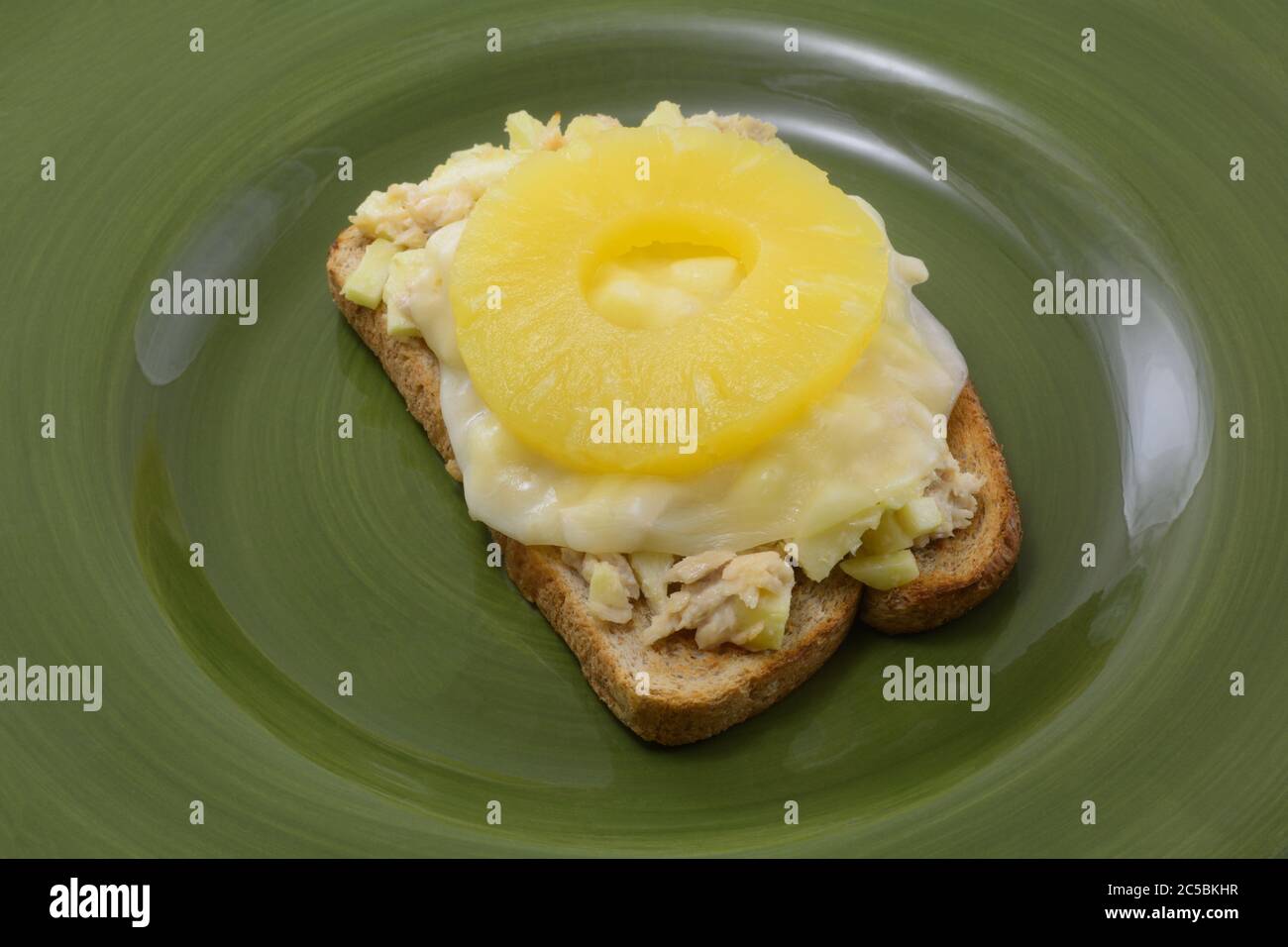 Panino aperto con insalata di tonno con fetta di provolone fuso e anello di frutta all'ananas Foto Stock