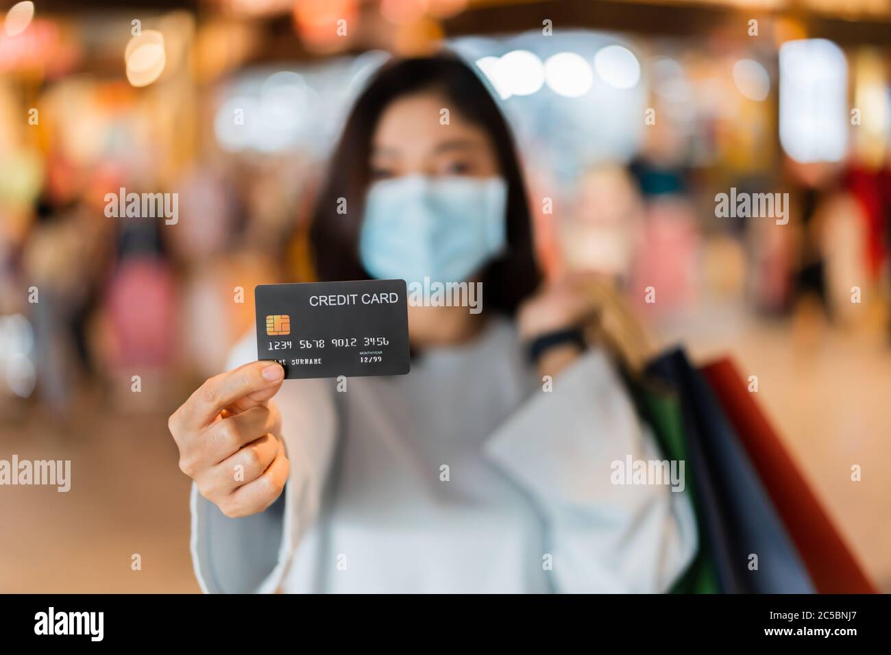 Carta di credito con giovane donna che indossa una maschera medica al centro commerciale per la prevenzione da coronavirus (Covid-19) pandemia. Nuovi concetti normali Foto Stock