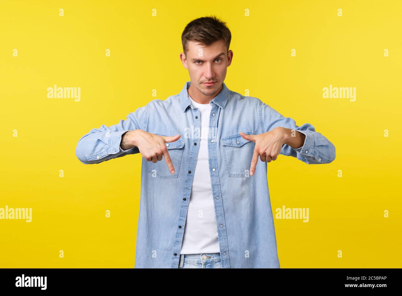 Bell'uomo biondo dall'aspetto serio che dà un suggerimento, puntando le dita verso il basso e guardando la fotocamera determinato, sguardo assertivo, informare la gente circa promo Foto Stock
