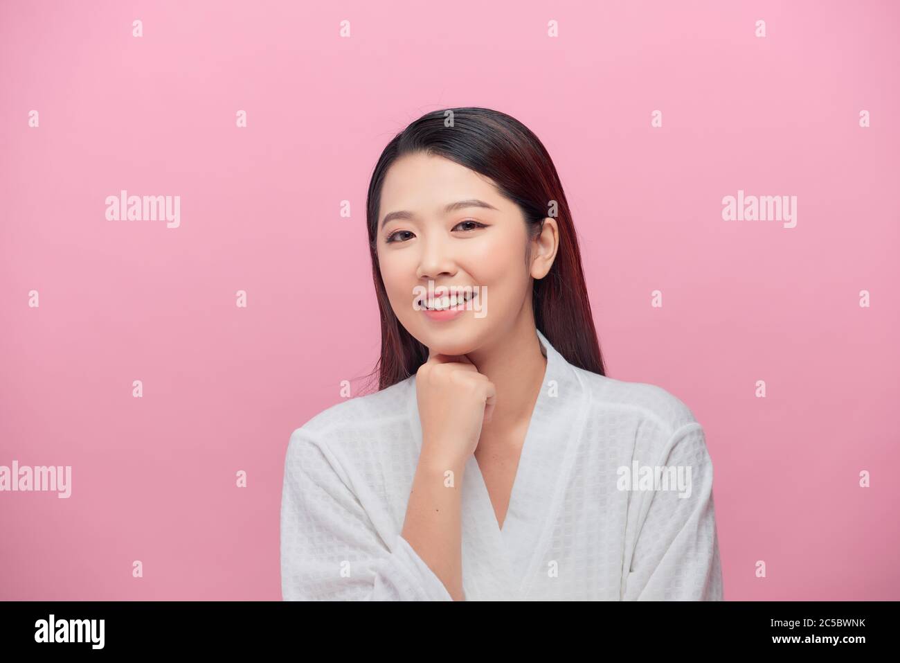 Donna affascinante con pelle pulita sorridente con denti bianchi, tenendo le mani sotto il mento su sfondo rosa Foto Stock
