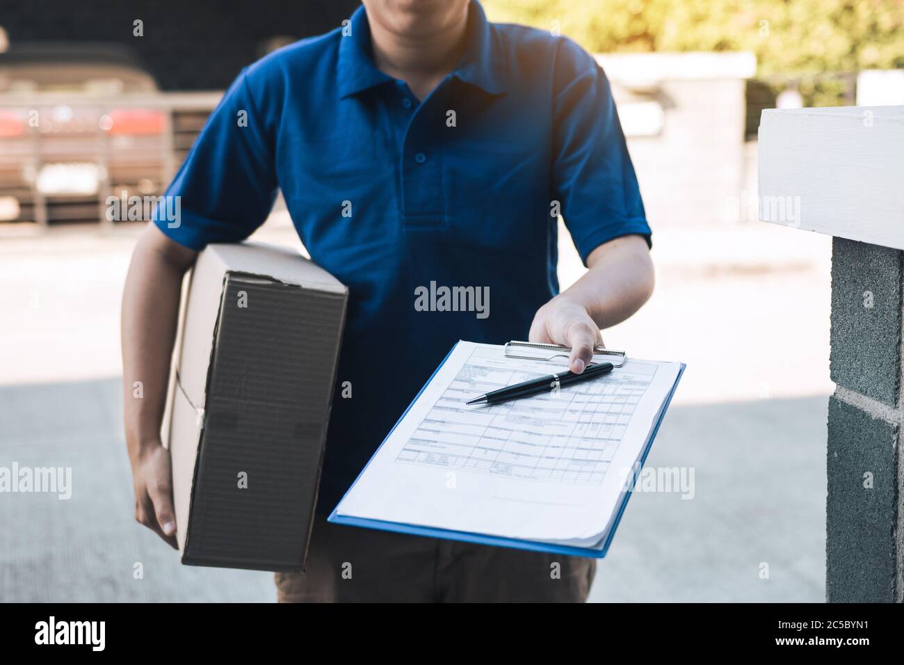 Giovane asiatico sorridente mentre consegnando una scatola di cartone alla donna che tiene il documento alla firma firma. Foto Stock