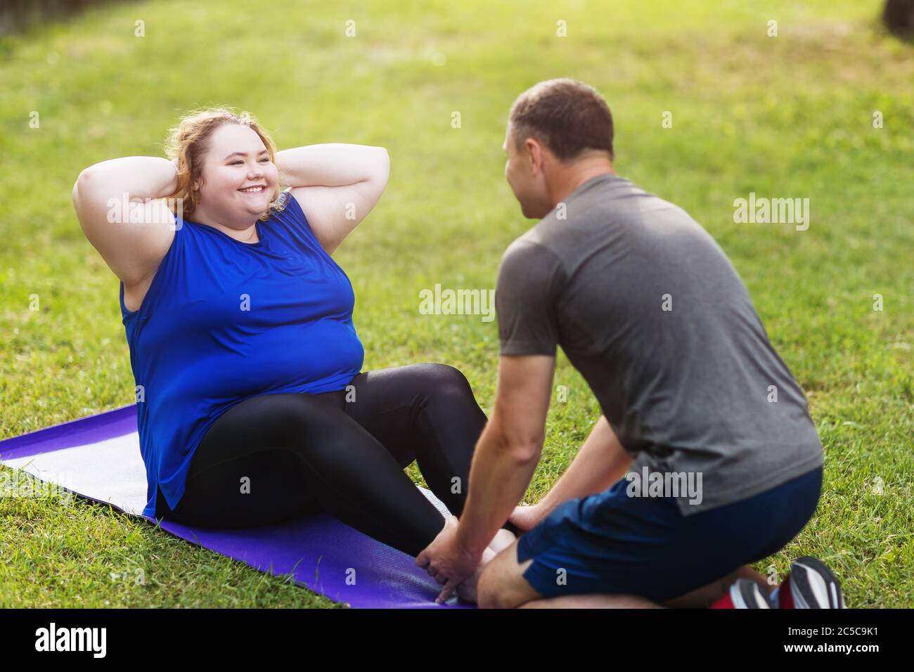 La taglia più giovane della bionda, esegue un'esercitazione esterna con un addestratore. Concetto di stile di vita sano Foto Stock