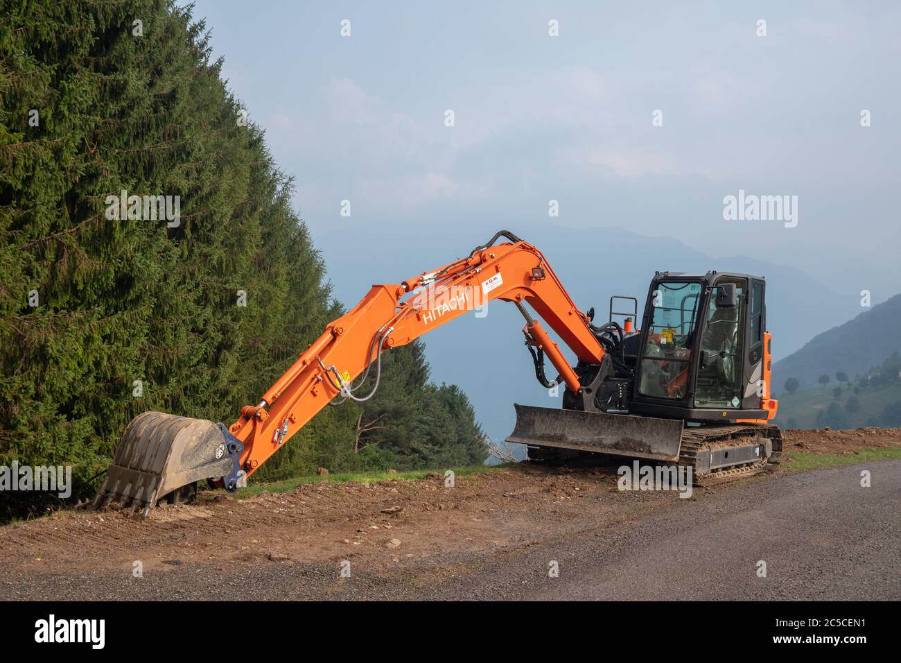 Escavatore cingolato Hitachi parcheggiato su una strada di alta montagna di  nuova costruzione contro una verde foresta di conifere sullo sfondo,  Lombardia, Italia Foto stock - Alamy