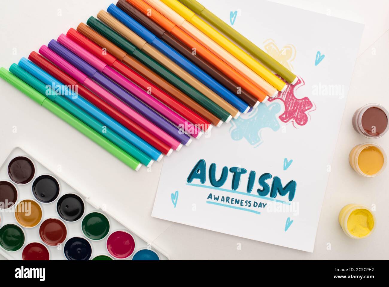 Vista dall'alto della carta con lettere autismo Awareness Day e pittura di puzzle su bianco con pennarelli e vernici Foto Stock