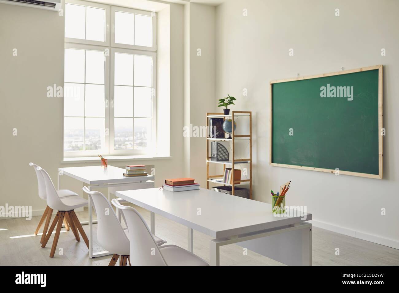 Scuola bianca interno classe. Luminosa sala da pranzo con finestre tavoli sedie tavola verde Foto Stock