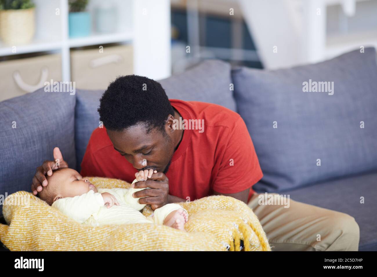 Padre africano baciando la mano del neonato mentre dormiva sono nel soggiorno di casa Foto Stock