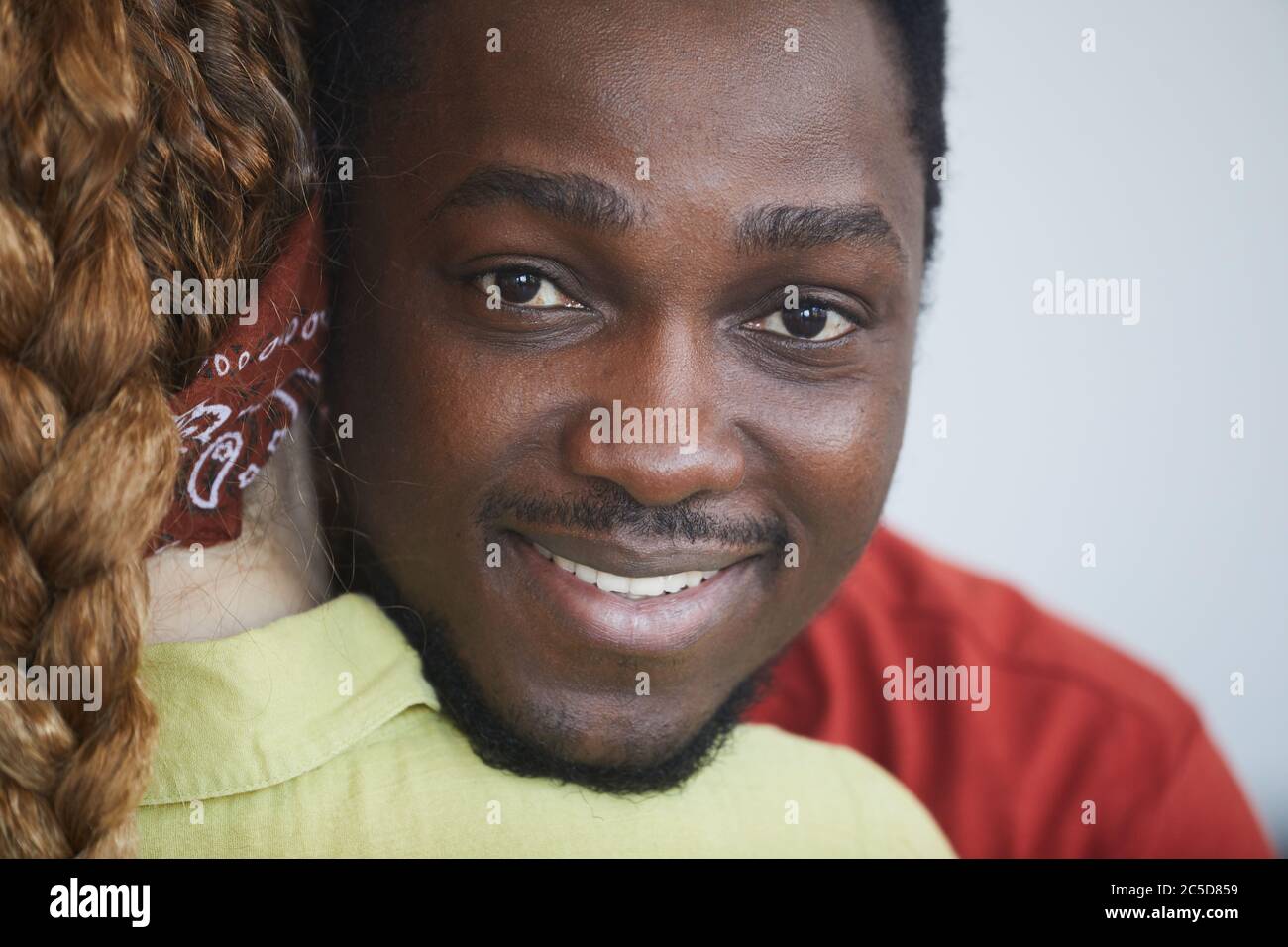 Ritratto di giovane africano abbracciando la donna e sorridendo alla macchina fotografica Foto Stock