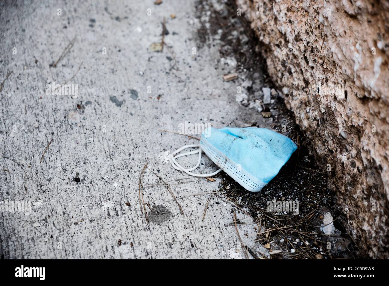 primo piano di una maschera chirurgica blu usata gettata sull'asfalto sporco di una strada, accanto al marciapiede Foto Stock